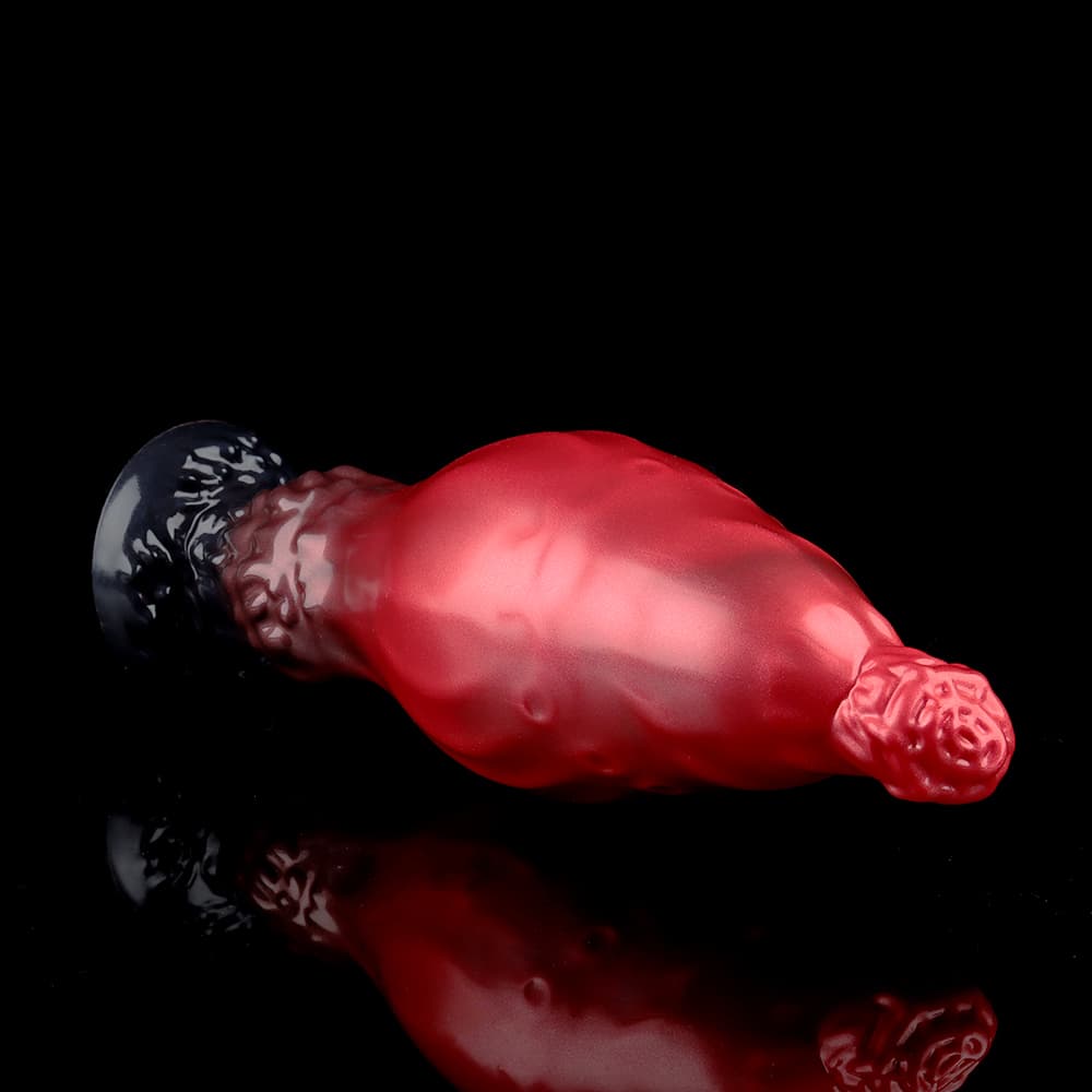 Close-up profile of the red and black monster fantasy dildo laying horizontally, highlighting the textured skin compound material and the sturdy black suction cup base.