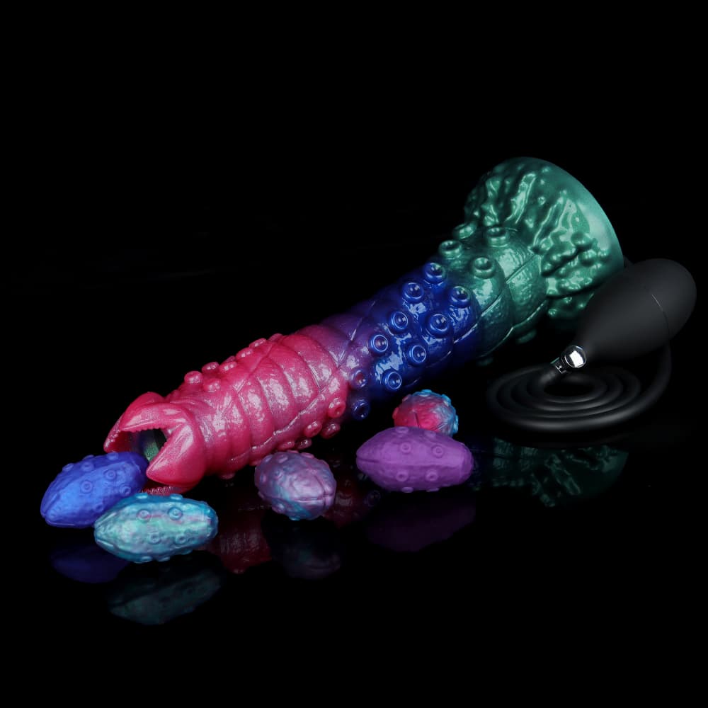 Tri-color alien egg layer dildo lying horizontally with realistic textured silicone monster eggs and a black manual squeeze bulb pump on a reflective black background.