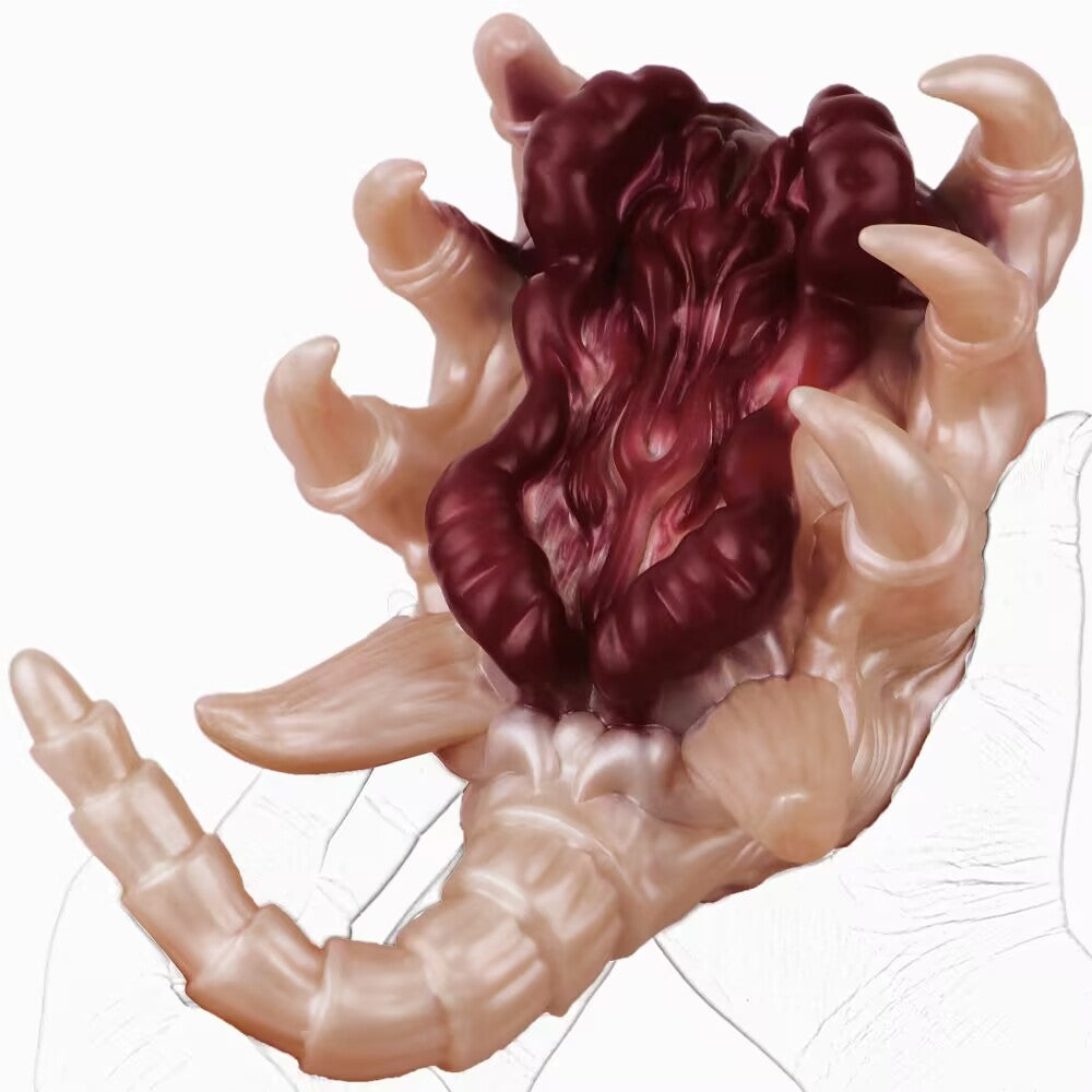 A full-length view of an Alien Facehugger-themed silicone stroker toy, with hands pulling the outer shell back to reveal the dark red intestinal texture. The toy is flesh-toned with defined