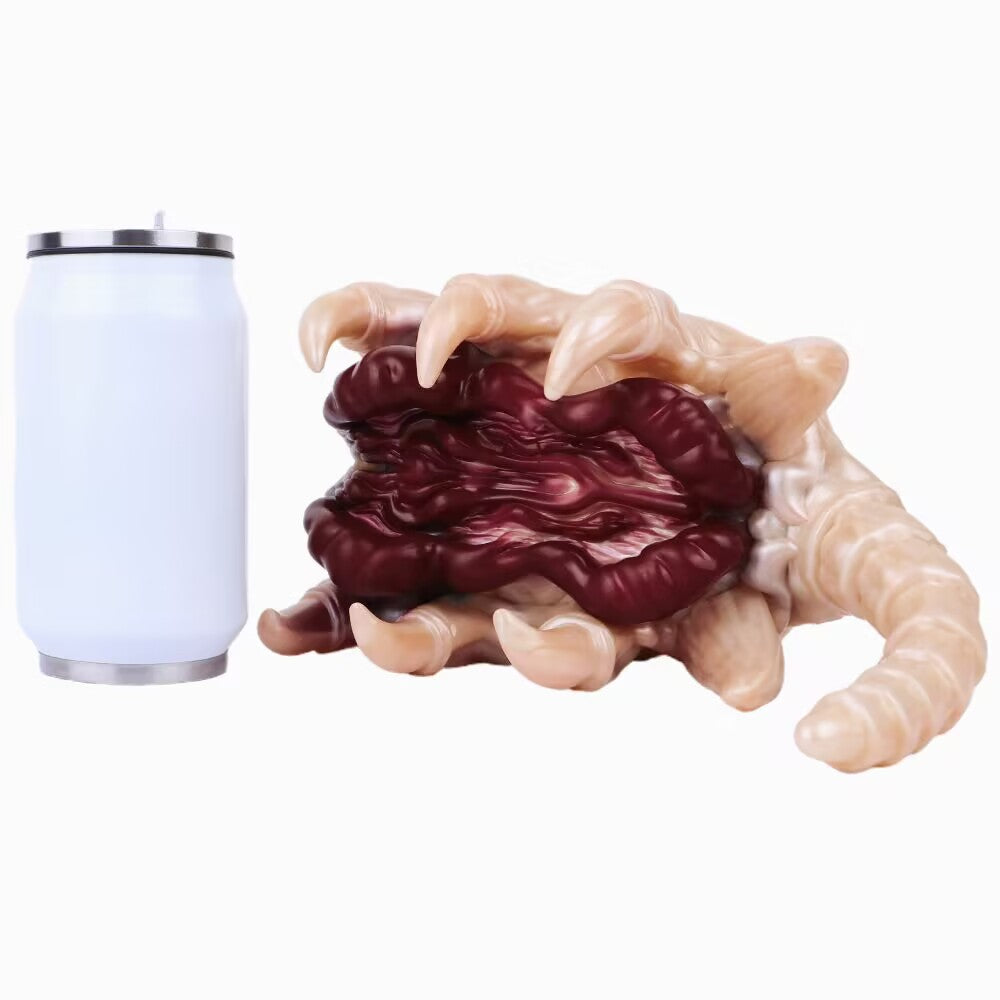 A Alien Facehugger-themed silicone stroker toy standing next to a standard metal soda can, providing a size comparison. The can is white and slightly shorter than the toy.