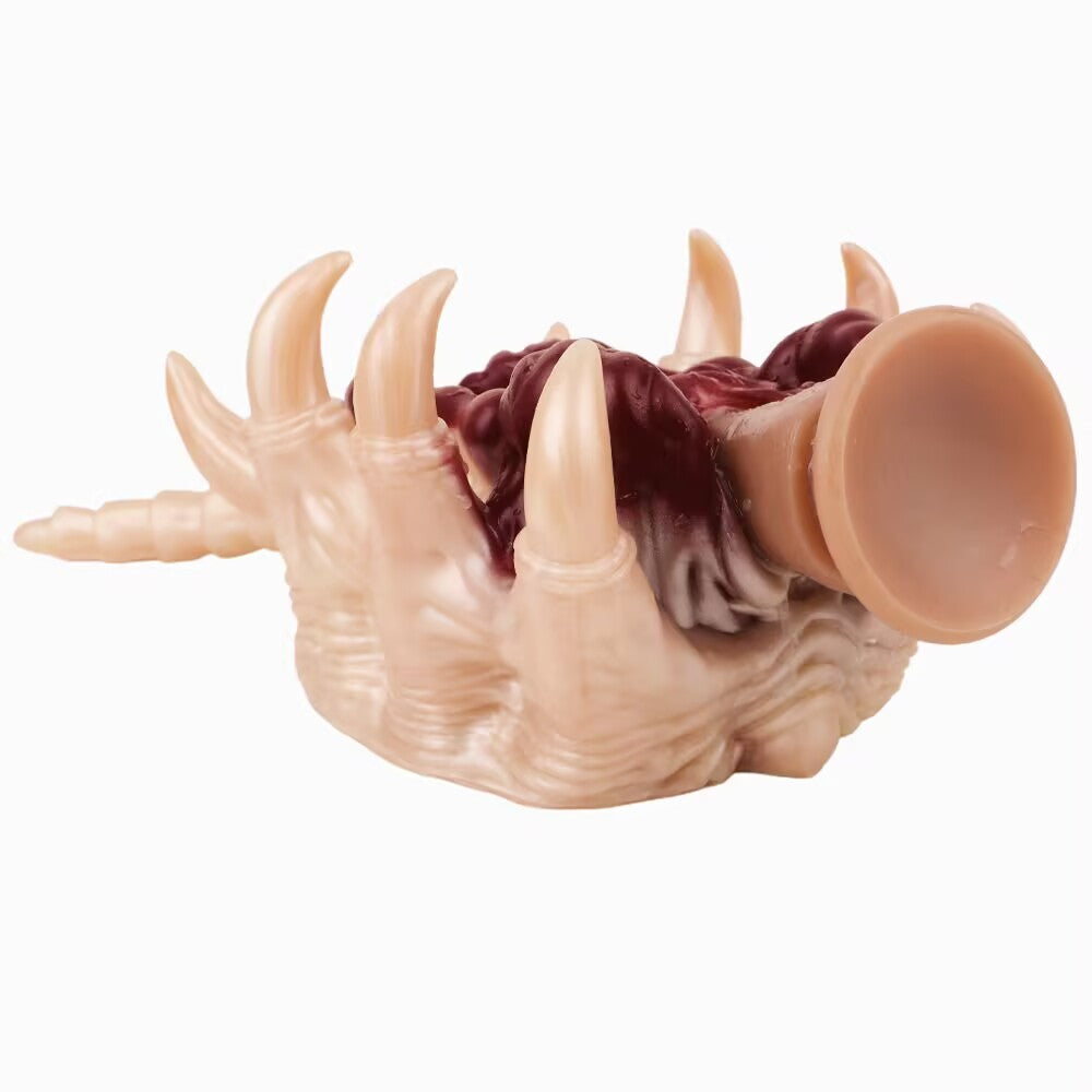 An Alien Facehugger-themed silicone stroker toy, showcasing its suction cup base at one end. The toy lies horizontally, showing its segmented tail and segmented claw-like edges.