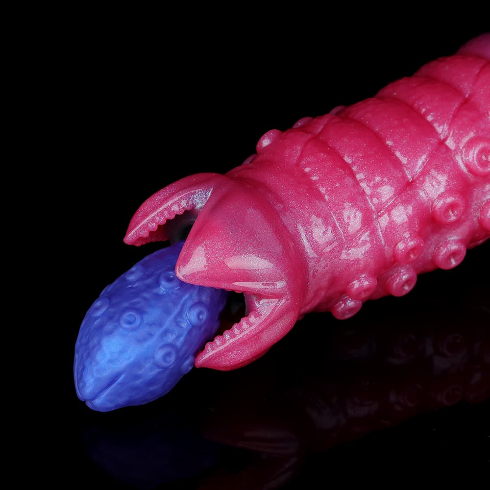 Macro close-up of the alien ovipositor dildo's pink claw-shaped tip dilating to deliver a blue textured silicone monster egg.