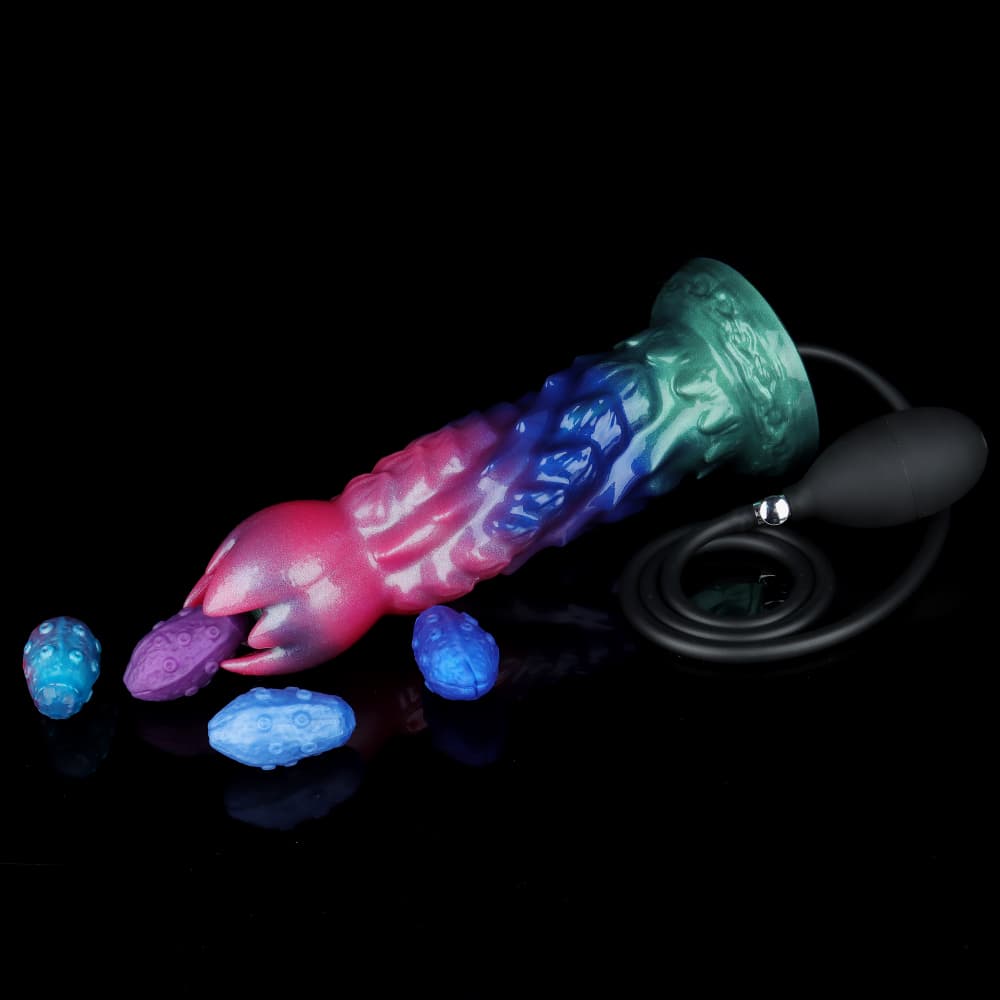 Shimmering green and purple alien ovipositor fantasy dildo lying horizontally on a black background, with four blue and purple textured egg refills and a black inflation bulb pump.