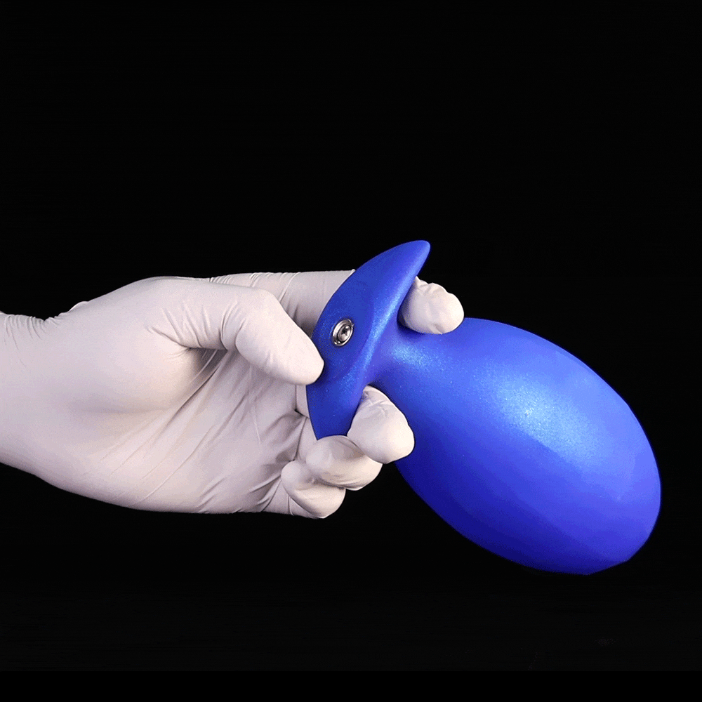 A hand in a white glove holding a light blue, smooth inflatable silicone butt plug with a metal air valve air pump connector against a black background.