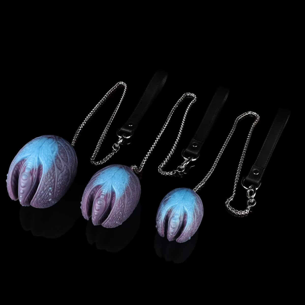 Alien fantasy egg silicone body beads with chains laid out on dark background.