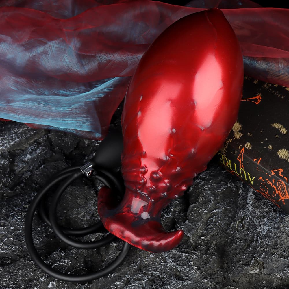 An inflatable red alien dildo with an inflation pump accessory, styled on a textured rock surface with gothic fabric decor.