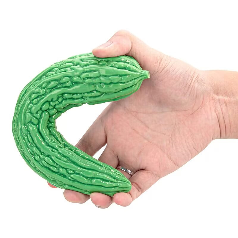 Hand flexing a green curved bitter gourd silicone dildo with realistic textured ridges for G-spot stimulation.