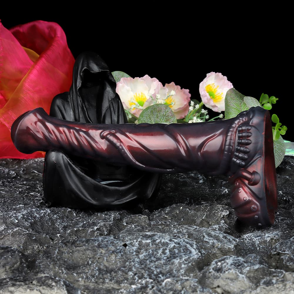 A large biomechanical cyberpunk dildo resting horizontally across a gothic hooded reaper statue surrounded by flowers.