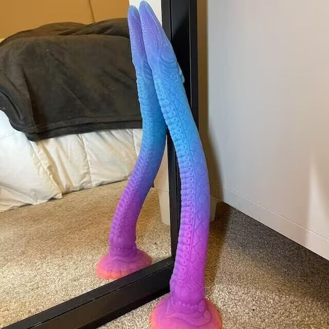 A multi-colored fantasy tentacle dildo attached to a bedroom floor mirror using its strong suction cup base, displaying hands-free play potential.