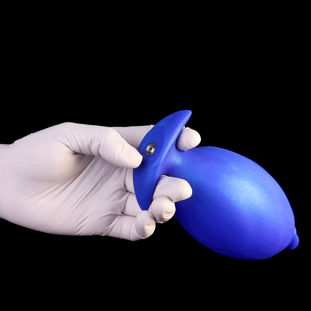 Gloved hand holding the blue flared base of an inflatable butt plug showing the premium metal air valve connection port. 