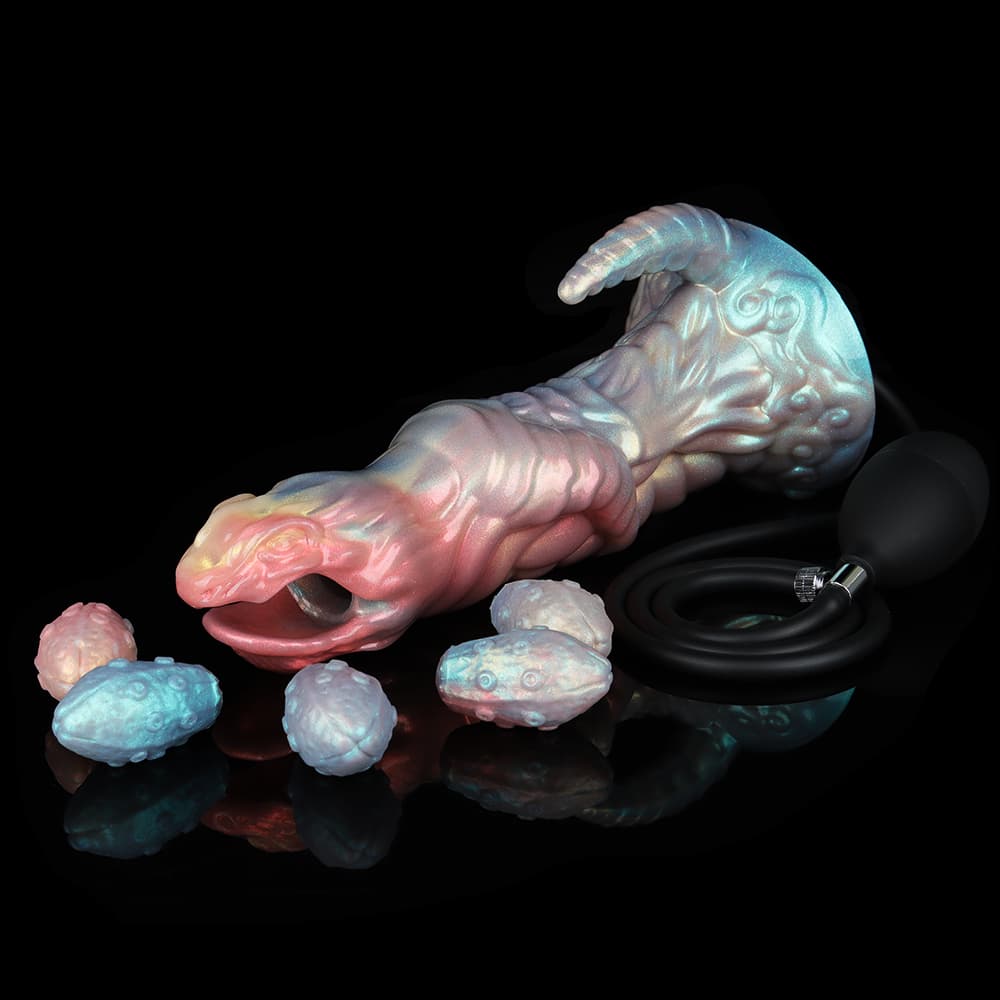 An iridescent pink and blue alien egg layer fantasy dildo lying horizontally on a black reflective surface, surrounded by 5 textured silicone eggs and a black inflation squeeze pump bulb.