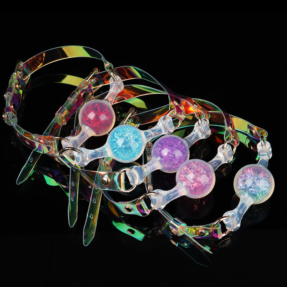 A stacked cluster of colorful silicone glitter mouth gags showing iridescent rainbow reflections on the PVC straps over a glossy black surface.