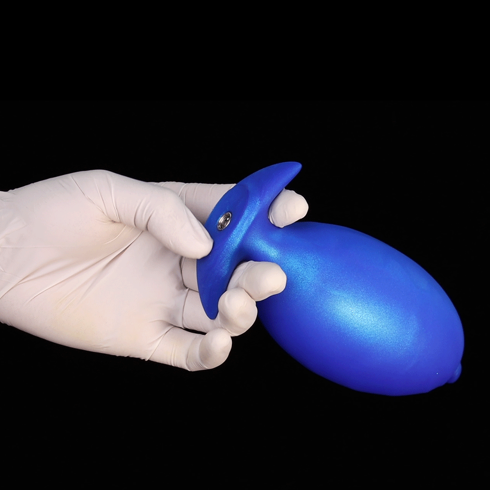 Hand wearing white glove holding a metallic blue sapphire inflatable butt plug showing the premium flared anchor base and textured surface against a dark background.