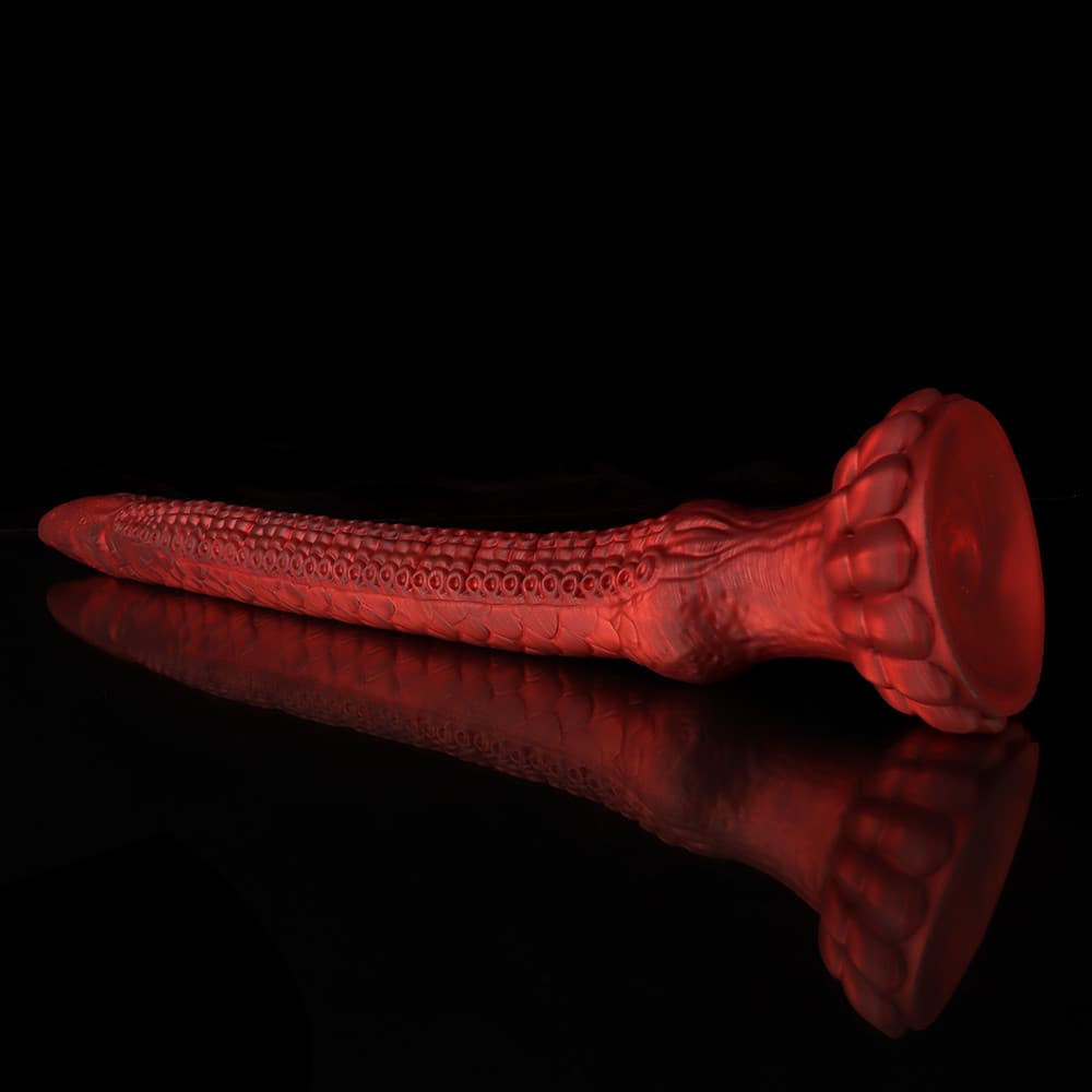 Side view of the translucent red monster dildo showcasing the powerful lotus-shaped suction cup base on a reflective black surface.