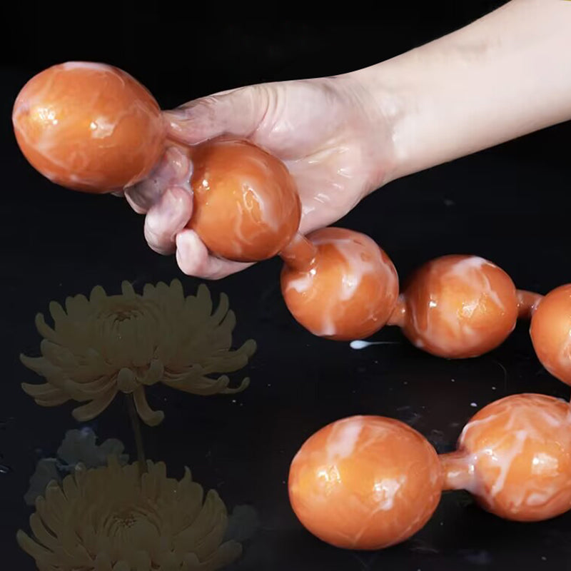 Hand holding flexible lubricated orange silicone anal beads string showing smooth texture.