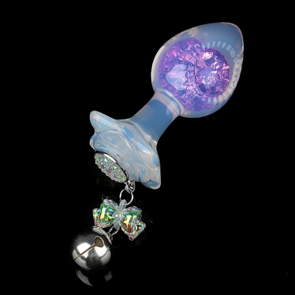 Opal glass butt plug with a purple crackle crystal core and a dangling silver bell charm against a black background.