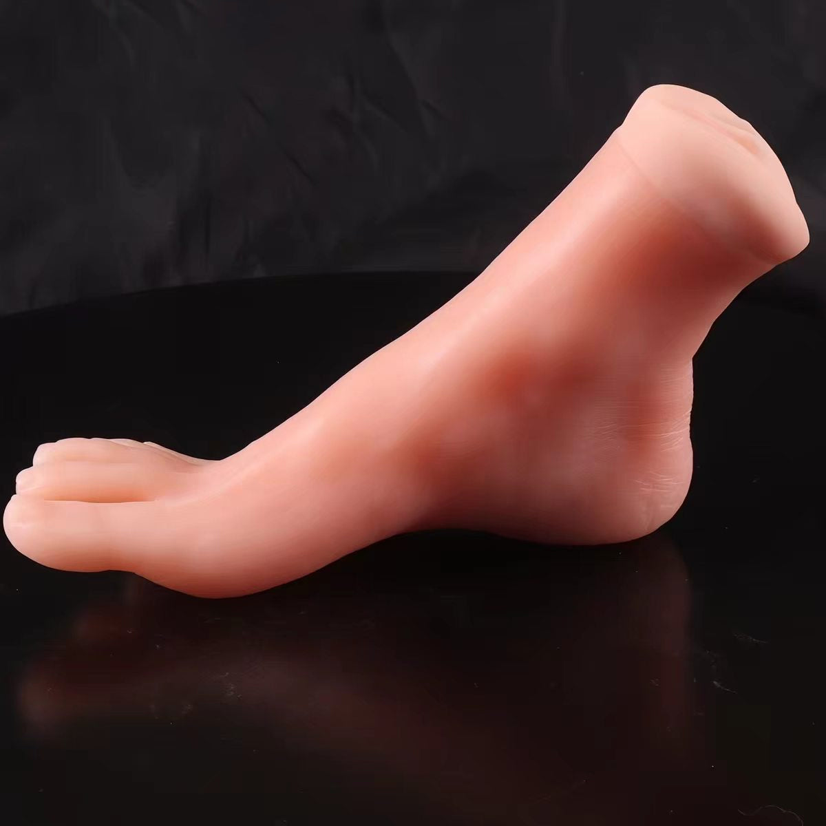 Side view of a realistic life-sized silicone model foot displayed on a reflective black background.