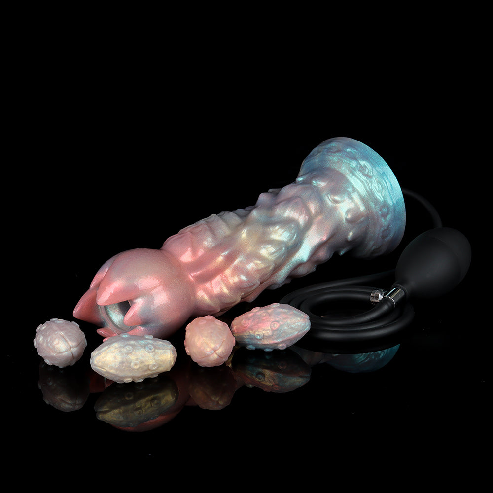 Shimmering pink and blue pearlescent alien ovipositor dildo lying horizontally next to fantasy textured silicone eggs and a black manual latex air pump with metal valve on a reflective black background.