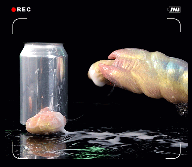 Shimmering pink and blue pearlescent alien ovipositor dildo lying horizontally next to fantasy textured silicone eggs and a black manual latex air pump with metal valve on a reflective black background.