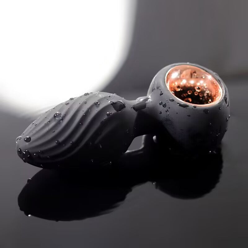 Silicone butt plug with rose gold metallic base retrieval ring resting on wet reflective surface