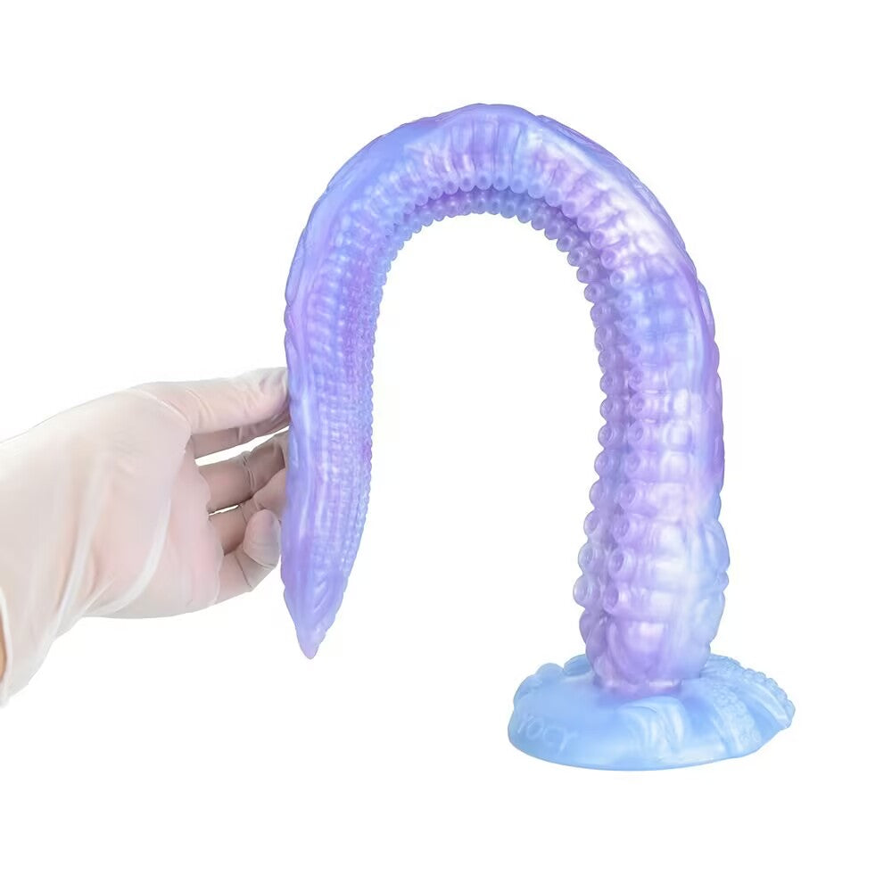 A purple alien tentacle dildo standing firmly on its suction cup base, forming an arch shape while being touched by a gloved hand.