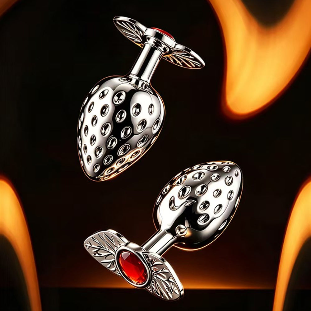 Floating view of strawberry metallic anal plugs showing the unique leaf-shaped flared base with a brilliant red crystal gemstone inset.
